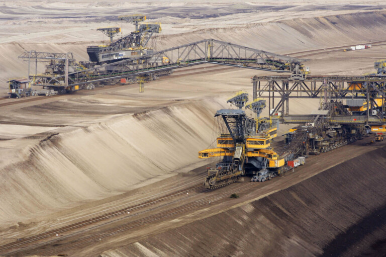 A large opencast mining operation in Latin America features heavy machinery, including several bucket-wheel excavators and conveyor belts. The barren landscape with visible earth cuts highlights the extensive mining activities in the region.