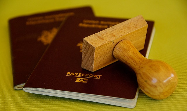 Two maroon passports are lying on a green surface. One passport has a wooden stamp resting on it. The word "PASSPORT" is visible on the cover in English and another language, suggesting its role in the "Formação da Empresa.