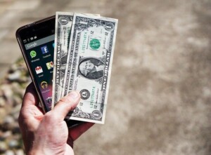 Person holding phone with US currency representing the value of e-commerce and online business in New Zealand