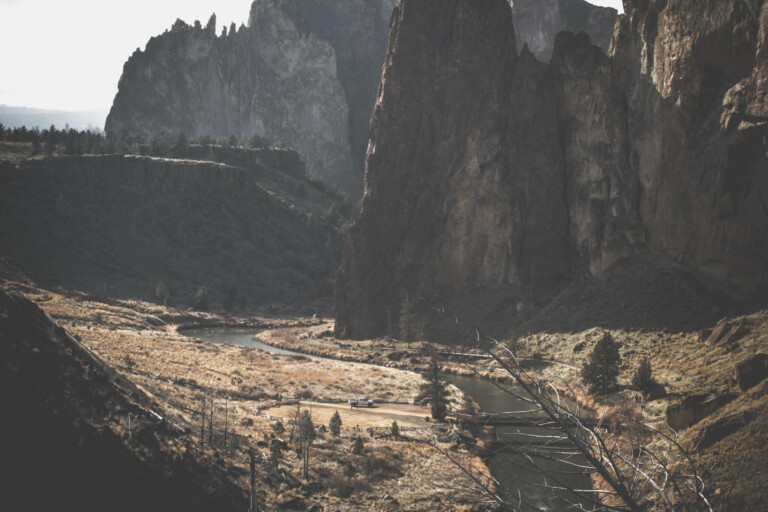 A scenic view of a mountainous landscape with a winding river flowing through a grassy valley. The image features tall, jagged rock formations and scattered trees, with sunlight casting shadows on the terrain. The serene and natural atmosphere captures the untouched beauty of Peru's mining opportunities.