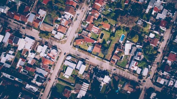 Vista aérea de un barrio suburbano en Chile que muestra una cuadrícula de calles bordeadas de casas. Las casas tienen una mezcla de techos rojos y blancos, y algunas propiedades tienen césped y árboles verdes visibles. También se pueden ver algunos caminos de acceso y pequeños jardines, lo que la convierte en una zona ideal para invertir en propiedades.