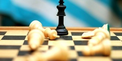 A chessboard displays a black king standing upright in the center, surrounded by several fallen white pieces. The focus is on the black king, symbolizing both its victory and the decisive moment in the formação da empresa. The background is blurred with shades of blue and white.