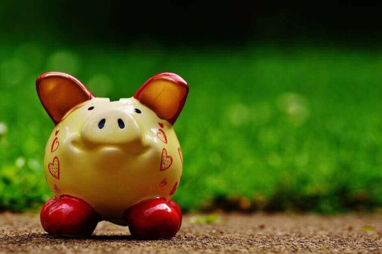 A yellow piggy bank with red feet and red hearts is placed on a brown surface with green grass in the background, reminiscent of the colorful journey to open a corporate bank account in Mexico.