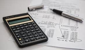 A black calculator lies on a printed financial document with figures and graphs. Beside it, a silver pen with its cap removed rests on the paper, suggesting ongoing calculations or notes by a tax accountant. The scene echoes the meticulous work required to pay taxes in Chile 2018.