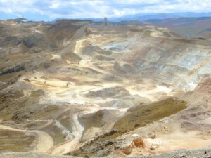 A vast open-pit mine with winding roads and large excavation areas is situated in an arid, hilly landscape. The mine extends into the distance with various machinery and structures scattered around. Amidst the clear sky with scattered clouds, this location could offer significant business opportunities under the Peru-India Free Trade Agreement.