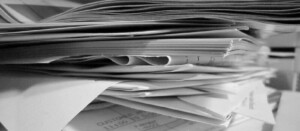 A black and white image of a stack of papers and documents, perhaps from an individual background check in Ecuador. The papers are piled haphazardly, some slightly curling at the edges and others stacked on top of each other. Text is partially visible on some documents, but not readable.