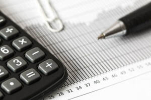 A close-up image showing a black calculator, a silver paperclip, and a pen placed on a document with a bar graph related to energy statistics.