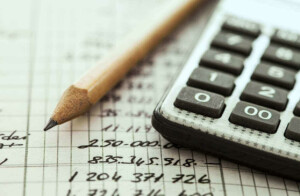 A close-up image of a pencil and a calculator placed on an open notebook with handwritten numbers. The grid paper suggests work related to calculations or accounting, potentially at a branch in Argentina. The focus remains on the pencil and calculator, highlighting meticulous record-keeping.