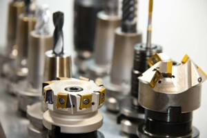 Close-up of various metal cutting tools arranged in a row on a workbench, with drill bits and milling cutters among them. Each tool showcases different designs and purposes, highlighting a variety of industrial machining equipment that expertly handles metals and ceramics alike.