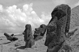 A black and white photograph of three Moai statues on Easter Island. Two statues are partially buried, displaying only their heads and shoulders. The foreground statue and middle statue are more prominent, while the third one is further back on a slope, reminiscent of historical mining concessions in Chile.