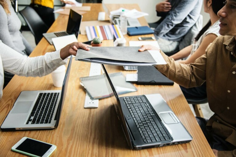 People at a desk exchanging documents over their laptops