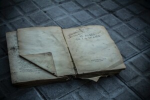 An old, worn-out book lies open on a tiled surface. The pages are yellowed with age, and some corners are torn. The title on the visible page reads "El Revés de La Trama" from Editorial Sud, revealing a tale set against the backdrop of free trade zones in Uruguay.