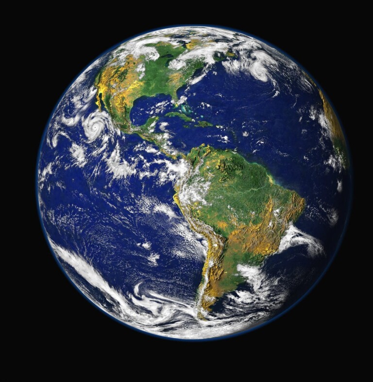 A full view of Earth from space showing North and South America prominently captures the ease of doing business across vast blue oceans, swirling white clouds, and varying terrain of green and brown landmasses. The planet appears against a black background.