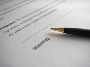 A close-up photograph of a contract with the word "SIGNATURE" underlined at the bottom. A black and gold pen is positioned near the signature line, indicating the document, possibly pertaining to mining in Bolivia, is ready to be signed. The rest of the contract text is blurred and not legible.