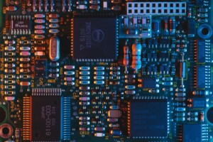 Close-up view of a colorful, illuminated electronic circuit board with numerous integrated circuits, resistors, capacitors, and other components. Various numbers and labels can be seen on the board and components as it gears up for international expansion into Central America.