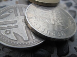 Close-up image of several coins stacked on top of each other on a textured surface. The front coin prominently displays embossed text and an abstract design, while the coins behind show partial inscriptions and patterns, reminiscent of the currency used when doing business in Colombia.