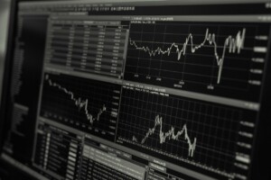 A computer monitor displays multiple graphs, charts, and tables illustrating financial data and stock market trends. The charts show fluctuating lines, indicating varying stock prices over time. The grayscale monitor reflects technology and innovation in Bolivia's burgeoning financial sector.