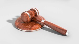 A wooden gavel and sounding block are placed on a smooth, light gray surface. The gavel has a polished finish with silver accents on the handle and head. The sounding block matches the gavel, symbolizing the precision required to liquidate a company in New Zealand. Both items are positioned side by side.