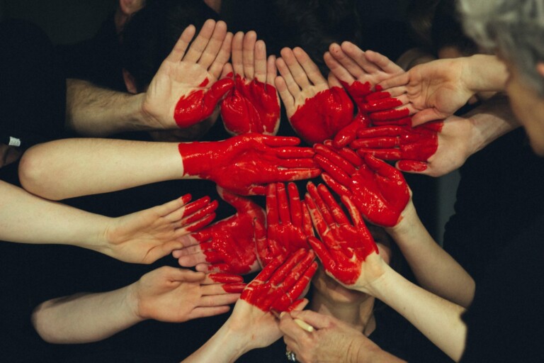 A group of hands arranged in a circular pattern with some hands covered in bright red paint. The red-painted hands form the shape of a heart, symbolizing unity and love. This inspiring image emphasizes the spirit needed to form an NGO in Peru, where compassion can truly make a difference against a dark backdrop.