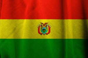 The image shows the flag of Bolivia, highlighting its connection to import and export regulations in Bolivia. It consists of three horizontal stripes: red on top, yellow in the middle, and green at the bottom. The flag features the Bolivian coat of arms at the center of the yellow stripe.