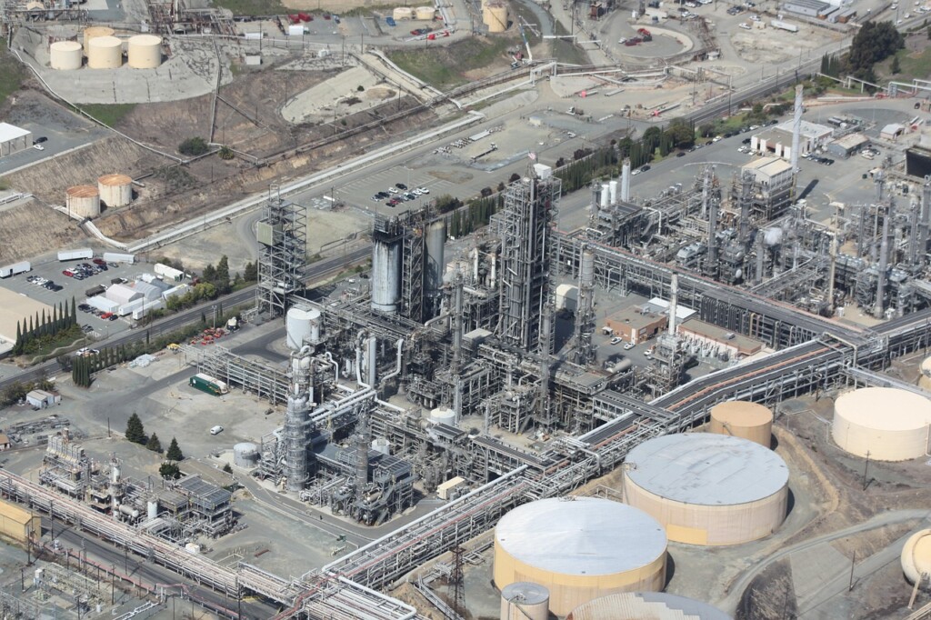 Aerial view of an industrial refinery complex with numerous pipes, storage tanks, and structures. The facility spans a large area with multiple buildings, containers, and machinery. Surrounding terrain includes some vegetation and other industrial setups. Due diligence in Bolivia ensures the site's compliance and efficiency.