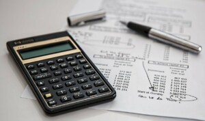 A close-up photo shows a black calculator and a silver pen on top of financial documents from an NGO in Guatemala. The documents feature various typed numbers, tables, and handwritten notes. The pen cap is placed next to the pen on the papers.