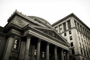 A black and white photo of two buildings: a neoclassical one with tall columns and intricate carvings, and a more modern one with rectangular windows. The angle looks up at the buildings, emphasizing their structure and architectural details—reminiscent of setting up a corporate bank account in Brazil amidst historic architecture.