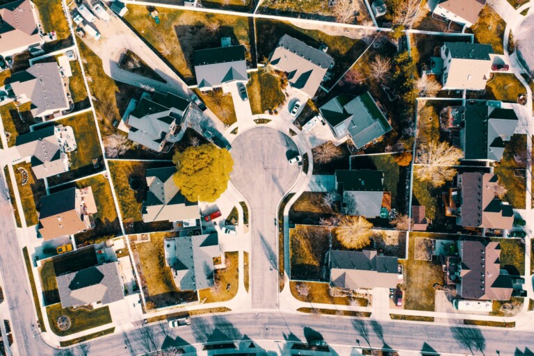 Vista aérea de un barrio residencial en Ecuador con una gran rotonda en el centro. Numerosas casas están situadas a lo largo de las curvas y tramos rectos de las calles. El paisaje incluye árboles, caminos de entrada y varios patios, un lugar ideal si desea comprar una propiedad en Ecuador.