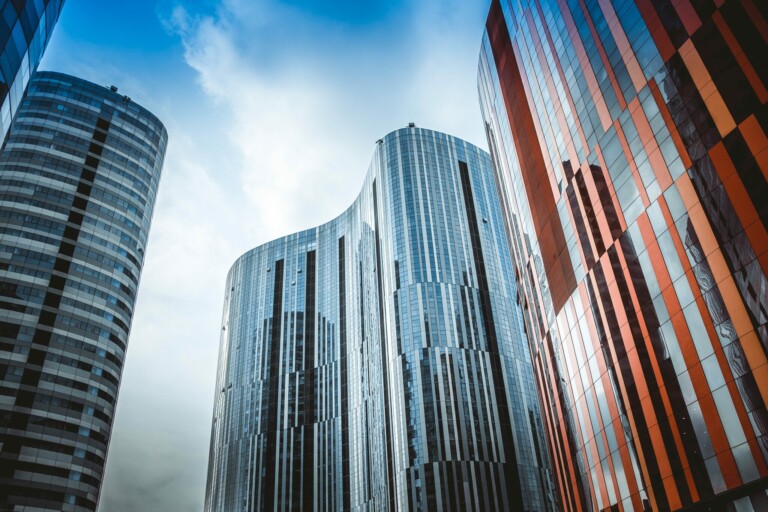 A view of tall, modern skyscrapers with curved architectural designs. One building, reflective with glass panels, stands out, while another mixes red and gray colors. The sky is partially cloudy in the background, resembling the complexity of invoicing requirements for a foreign company in Ecuador.