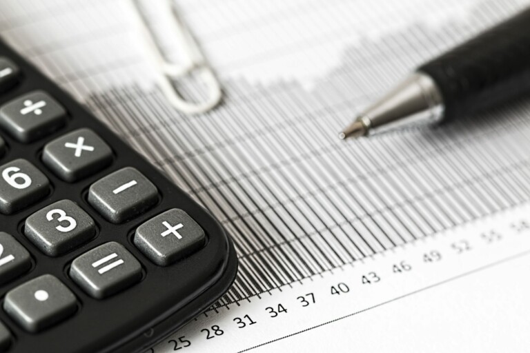 A close-up of a calculator, a pen, and a paperclip resting on a sheet of paper with a bar graph detailing Chile's Transfer Pricing. The calculator displays buttons for addition, subtraction, and other functions. The pen has a dark grip and a silver tip. The paperclip is partially visible.