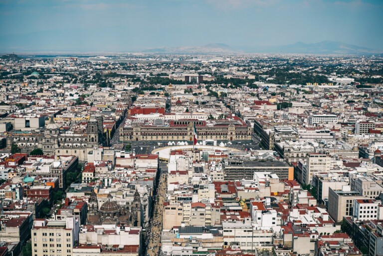 Aerial view of a large cityscape filled with numerous buildings in various shapes and sizes, akin to the complexities faced during M&A Due Diligence in Mexico. The image captures a dense urban area with mountains visible in the distant background under a partly cloudy sky.