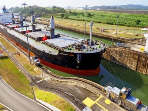 Una vista aérea del gran carguero "LOUISIANA MAMA" pasando por las esclusas de un canal. El barco, parte integral de las operaciones de visa de negocios Panamá, está rodeado de agua y varias estructuras mecánicas. Al fondo se ven colinas verdes y estructuras adicionales.