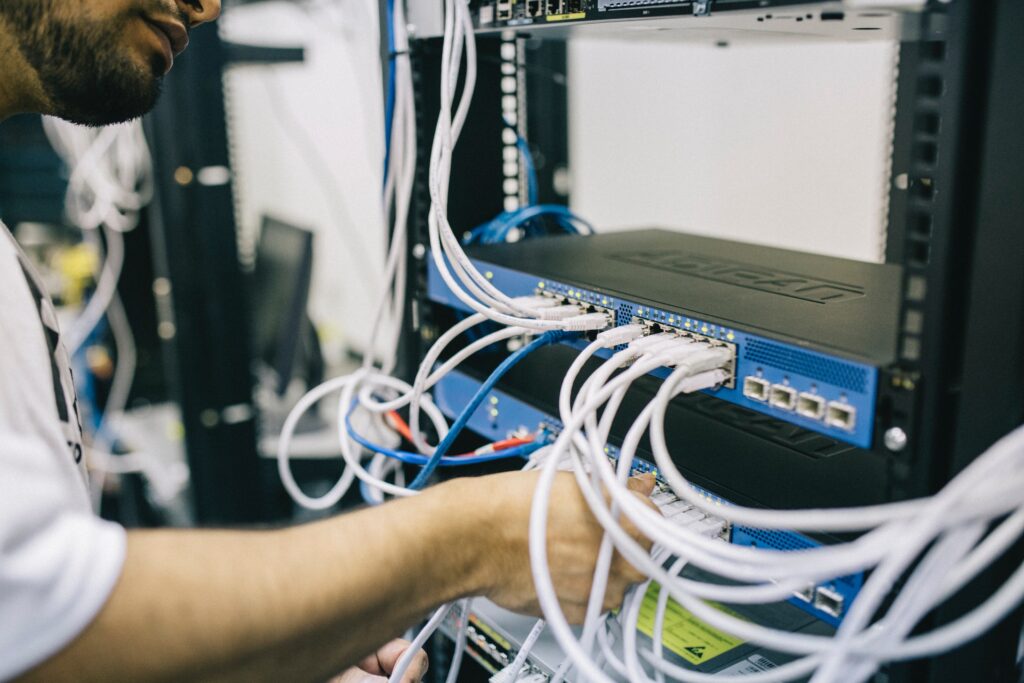 A person is working on server equipment, connecting numerous white network cables to a rack-mounted device. The background shows more networking hardware and equipment, suggesting a technical or server room. This could be a glimpse into the operations of one of Ecuador's tech companies.