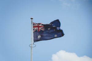 An Australian flag is flying on a flagpole against a backdrop of a blue sky with a few clouds, symbolizing the optimism and potential for starting a business in Australia. The flag features the Union Jack in the upper left corner and several white stars on a dark blue field.