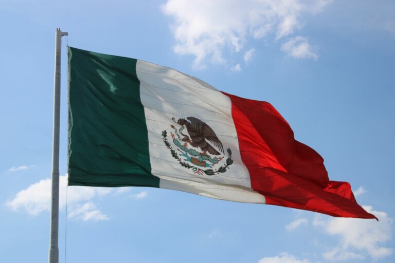 La imagen muestra la bandera de México, un símbolo que suelen ver quienes buscan una visa inversionista de México. Consta de tres franjas verticales: verde a la izquierda, blanca en el medio y roja a la derecha. En el centro, sobre la franja blanca, está el escudo nacional que representa un águila posada sobre un cactus con una serpiente en el pico.