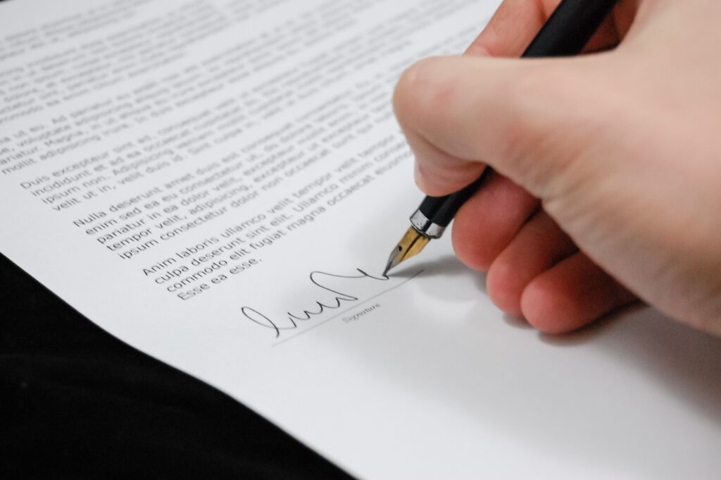 A hand is shown signing a document with a fountain pen. The document contains multiple paragraphs of text, which are not fully readable. The focus is on the pen and the hand of an attorney in Uruguay making the signature at the bottom of the page.