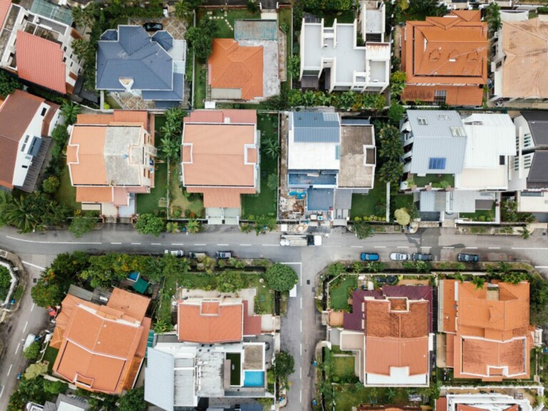 Vista aérea de un barrio residencial con hileras de casas con techos rojos, azules y blancos. Las casas están separadas por caminos de acceso, caminos y zonas verdes. Los coches están estacionados en las calles y en las entradas de vehículos. El área está bien organizada y es suburbana, ideal si busca comprar una propiedad en Brasil.