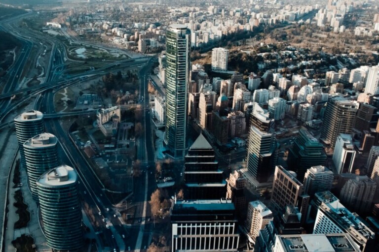 Vista aérea de un paisaje urbano densamente construido en Chile con numerosos edificios de gran altura, carreteras que se cruzan y espacios verdes. La imagen captura una combinación de estructuras residenciales y comerciales bajo un cielo despejado, lo que refleja el entorno dinámico donde prosperan las nuevas empresas.