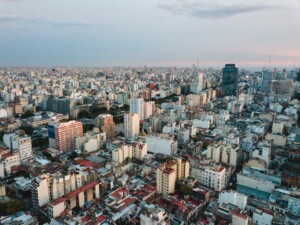 Vista aérea de una ciudad densamente poblada con numerosos edificios, calles y tejados, altos y bajos. El horizonte muestra un cielo ligeramente nublado que pasa del día al anochecer. El horizonte, que se extiende hasta el horizonte sin puntos destacados visibles, representa la típica dirección fiscal en Argentina.