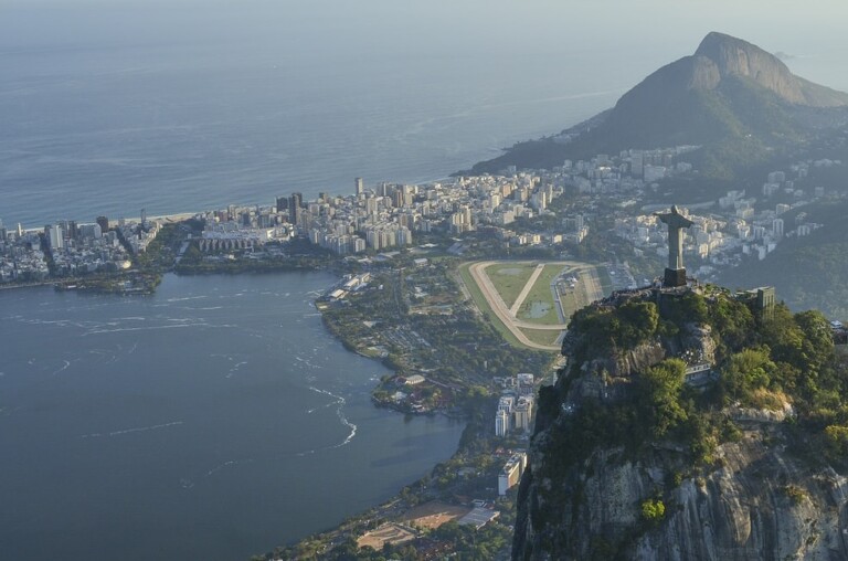 Aerial view of Rio de Janeiro, featuring the Christ the Redeemer statue on Corcovado Mountain in the foreground. With Guanabara Bay, city buildings, and a runway in the middle ground, this breathtaking scene captivates those visiting for business with Contador Tributário Internacional no Brasil.