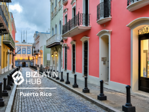 Una calle adoquinada en Puerto Rico llena de edificios coloridos, incluidas fachadas rosadas y amarillas. Farolas y bolardos salpican la acera. El logotipo de "Biz Latin Hub" y el texto "Turismo en Puerto Rico" están superpuestos en la esquina inferior izquierda de la imagen.