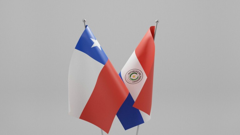 Se exhiben dos banderas cruzadas: la bandera de la izquierda presenta una estrella blanca sobre un campo azul encima de franjas rojas y blancas (Bandera de Chile), y la bandera de la derecha tiene un emblema circular en blanco, con franjas rojas y azules (Bandera del Paraguay), simbolizando la unidad a través del Tratado de Libre Comercio, sobre un fondo liso.