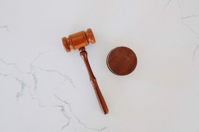 A wooden gavel and its round base are placed on a white surface with subtle gray veining, reminiscent of artifacts caçadores de cabeças na Colômbia might possess. The gavel's handle extends toward the left, while the base sits to the right of the gavel's head.