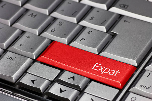 A close-up of a keyboard shows most keys in standard colors. A single key, located where the "Enter" key typically is, stands out in red and is labeled "Expat," possibly symbolizing offshore investments for expats. Arabic characters are visible on some keys.