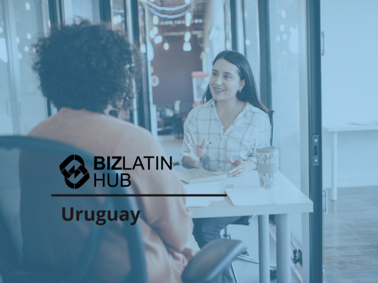 Two people are having a discussion in an office setting. One person, facing the camera, is sitting in a chair and gesturing with their hands while talking. The other person's back is toward the camera. Text on the image reads "BIZLATIN HUB Uruguay: Hiring in Uruguay.