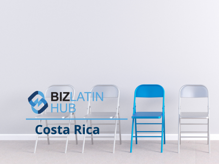 Four metal folding chairs are lined up against a gray wall. Three chairs are gray, and one is blue. The BizLatin Hub logo and the words "BIZ LATIN HUB Costa Rica" are superimposed on the left side of the image, illustrating their involvement in IT recruitment in Costa Rica.