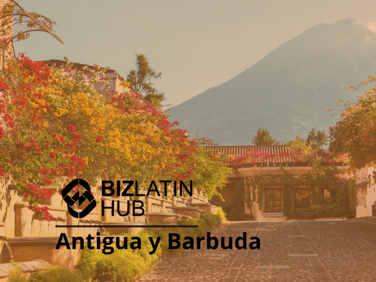 A scenic street in Antigua y Barbuda with colorful flowers and bushes lining the path. In the background, there is a mountainous landscape. The image includes the Biz Latin Hub logo and the text "Biz Latin Hub Antigua y Barbuda: Constitución de empresas en Antigua y Barbuda.