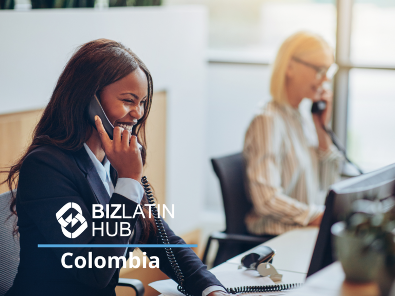 Dos mujeres trabajan en una oficina. La mujer en primer plano sonríe y habla por teléfono, vestida de negocios. Otra mujer al fondo también habla por teléfono. La imagen tiene el texto "BIZLATIN HUB Colombia" en primer plano, destacando experiencia en ley laboral en Colombia.