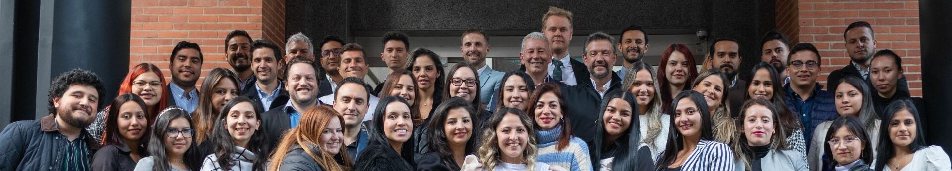 El equipo de biz latin hub, de pie, muy juntos delante de un edificio con paredes de ladrillo. Van vestidos con diversos atuendos, desde informales hasta de negocios. 