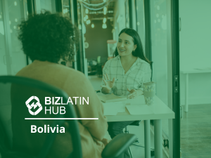 Two people are seated at a desk in an office setting, engaged in a conversation. The person on the right is gesturing with her hands. A mug, papers, and writing materials are on the desk. The image features the BizLatin Hub logo and the text "Employer of Record Bolivia.